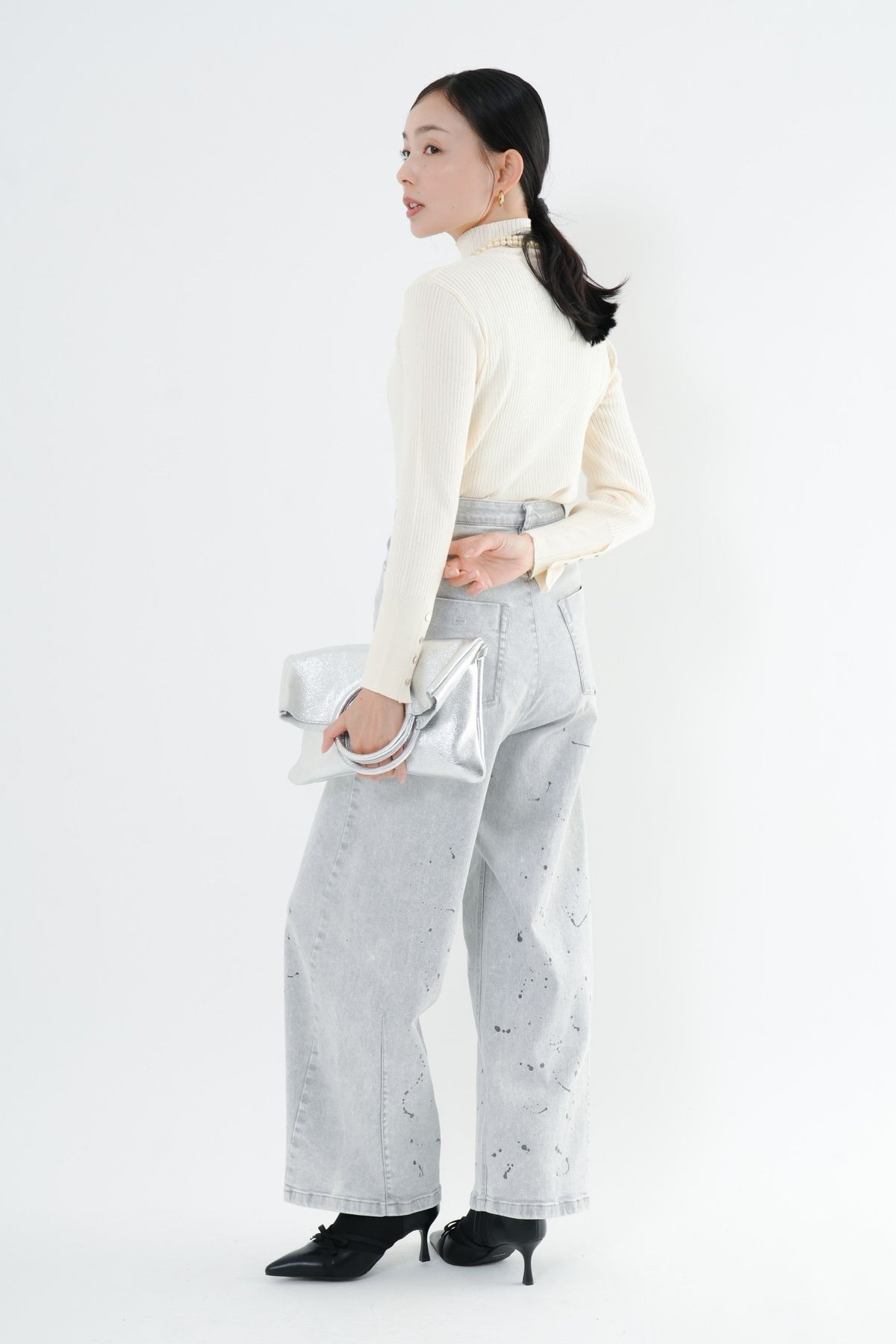 e-clothing-online storeのCLOCHEリブハイネックニットを着用した女性。袖口のゴールドボタンが特徴的な白のタートルネックニットに、ペイント加工のデニムを合わせた秋冬のきれいめスタイル。