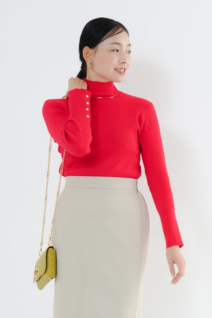 e-clothing-online storeのCLOCHEリブハイネックニットを着用した女性。袖口のゴールドボタンが特徴的な赤のリブニットにベージュのロングスカートを合わせたきれいめスタイル