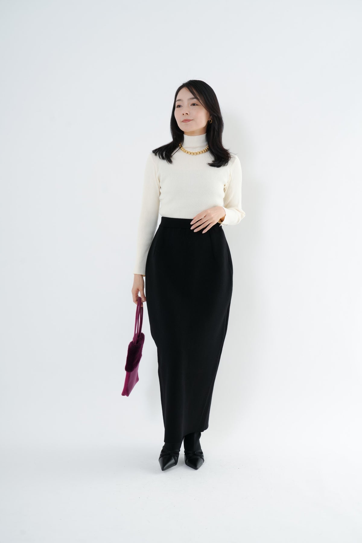 e-clothing-online storeのCLOCHEリブハイネックニットを着用した女性。ホワイトのタートルネックにブラックのロングスカートを合わせたきれいめなコーディネート。