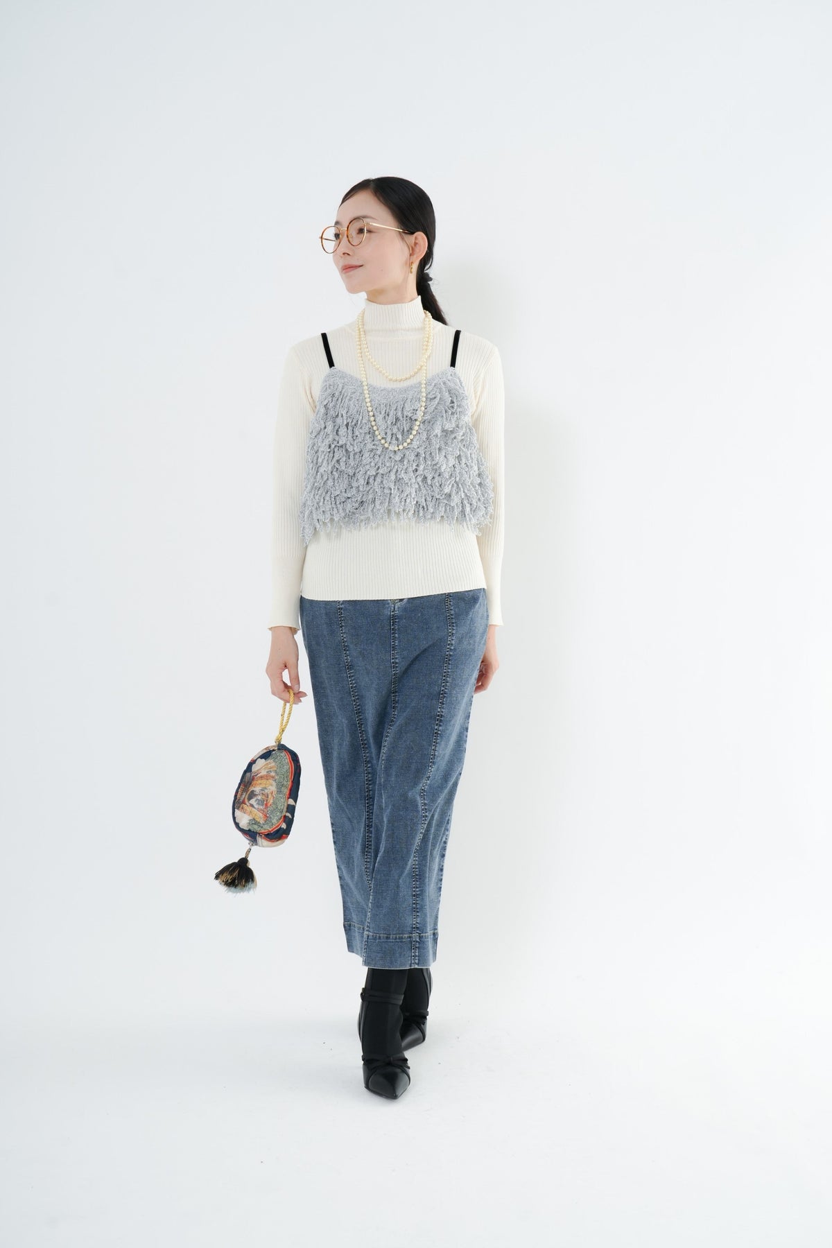 e-clothing-online storeのCLOCHEリブハイネックニットを着用した女性。白のタートルネックにグレーのフリンジキャミソールとデニムスカートを合わせたレイヤードスタイル。