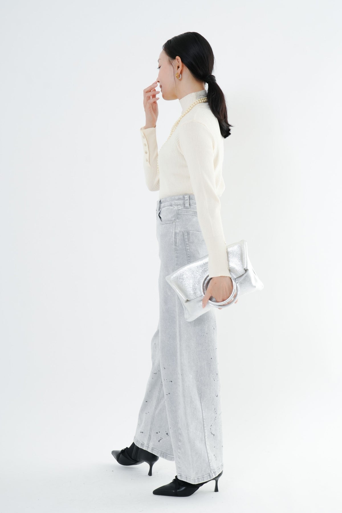 e-clothing-online storeのCLOCHEリブハイネックニットを着用した女性。袖口のゴールドボタンが特徴のホワイトニットに、ライトグレーのデニムとシルバーのバッグを合わせたきれいめコーデ