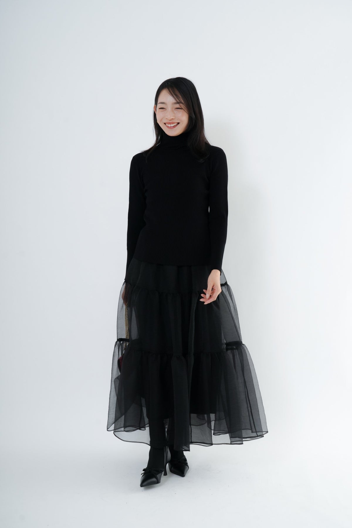 e-clothing-online storeのCLOCHEリブハイネックニットを着用した女性。黒のタートルネックニットに黒のチュールスカートを合わせた上品なコーディネート。