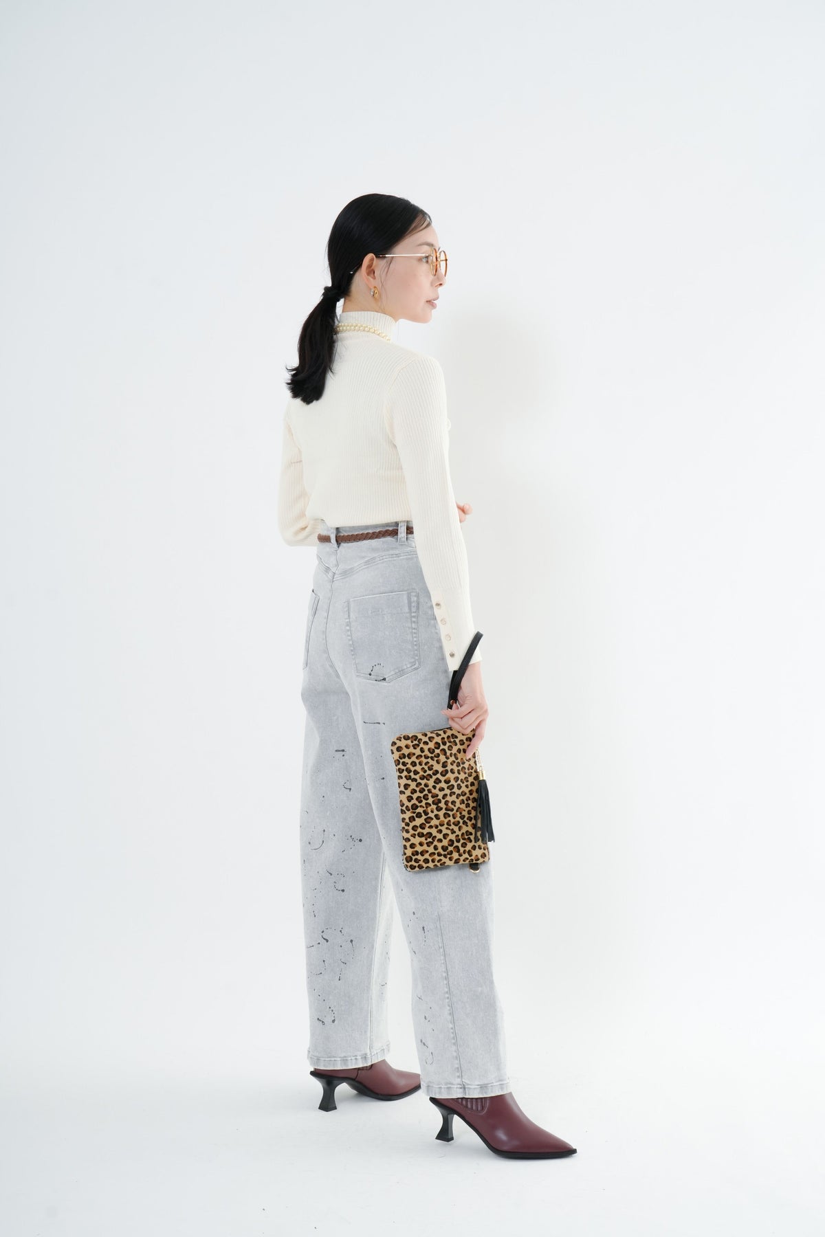e-clothing-online storeのCLOCHEリブハイネックニットを着用した女性。袖口のゴールドボタンが特徴のホワイトニットにデニムを合わせたコーディネート。