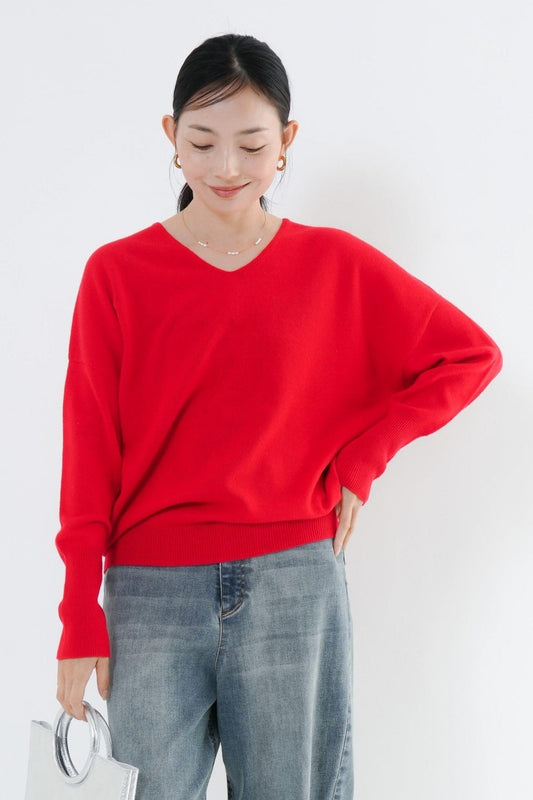 e-clothing-online storeの鮮やかな赤色のウール混Vネックニットを着用した女性。ゆったりとしたシルエットでデニムパンツと合わせたカジュアルなコーディネート。